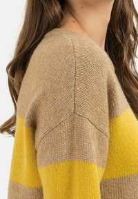 Brun og gul stribet sweater, lavet af et blødt strikkemateriale. Har en rund halsudskæring og skuldersøm detalje. Teksturen ser hyggelig ud.