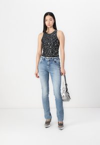 Haut sans manches noir à pois blancs, jeans ajustés bleu clair, sac à main argenté et chaussures métalliques à bouts pointus.