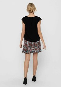 Černý krátký rukáv top s krajkovým lemem, doplněný květinovou sukní po kolena s červenými, modrými a zelenými květy na tmavém pozadí.