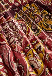 Tissu plié avec des motifs floraux paisley rouge, jaune, noir et blanc, créant une apparence stratifiée et texturée.