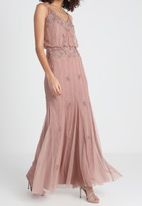Long evening dress in soft pink, featuring a layered top, intricate beadwork, and a flowing skirt. Adjustable straps and elegant design.