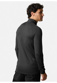Maglietta sportiva nera a maniche lunghe con colletto alto, caratterizzata da una texture liscia e da un design aderente, mostrata da una vista posteriore.