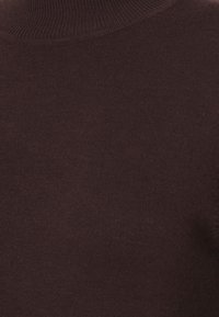 Lähikuva tummanruskeasta neulotusta kankaasta, jossa on ribbikaulus ja hieno, sileä rakenne.