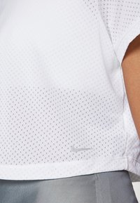 Top deportivo blanco de Nike con tejido de malla transpirable, mangas cortas, un dobladillo redondeado y un pequeño logo gris en la parte delantera.