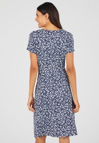 Abito blu navy con motivo floreale bianco, maniche corte e una leggera forma ad A. Il tessuto appare leggero e morbido al tatto.