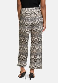 Wijduitlopende broek in een zigzagpatroon, met zwart, wit en aardetinten, gemaakt van lichte stof. Beschikt over een hoge tailleband.