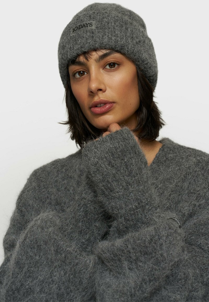 Gorro de punto gris y suéter de gran tamaño hecho de material suave y esponjoso. El gorro tiene una etiqueta con el logo; el suéter tiene mangas holgadas y texturizadas.