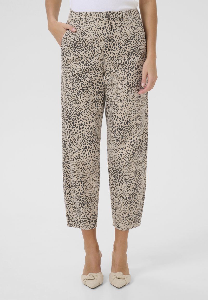 Pantalon beige, ample, présentant un motif léopard noir. Le design comprend des poches sur le devant et une coupe au niveau de la cheville.