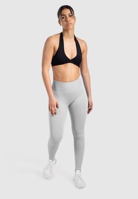 Soutien-gorge de sport noir à encolure halter associé à un legging taille haute gris clair, tous deux ajustés et extensibles, portés avec des chaussures de sport blanches.