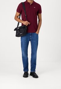 Maroon polo shirt, blue jeans, black shoulder bag, black shoes. The bag features a flap closure and adjustable strap. Casual outfit presentation.