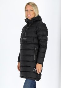 Svart puffjacka med hög krage, dragkedja framtill och sidofickor. Har horisontella, kviltade sektioner och en logotyp på den nedre fållen.