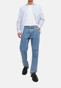 Lichtblauwe gestreepte shirt over een wit T-shirt, gecombineerd met rechte blauwe jeans en zwarte instappers. Casual outfit met een eenvoudig ontwerp.