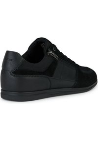 Zapatilla negra de corte bajo con paneles de cuero y tejido mixtos, cremallera lateral, cierre de cordones y suela delgada vista desde el lado exterior.