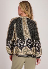 Langsleeve blouse in zwart, crème en groen met een ingewikkeld bloemenpatroon, gathered halslijn en subtiele ballonmouwen.