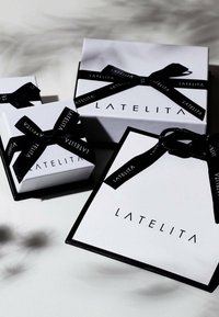 Tre hvide gaveæsker i forskellige størrelser, med sort bånd og "LATELITA" branding. Glat tekstur med kontrasterende sorte detaljer.