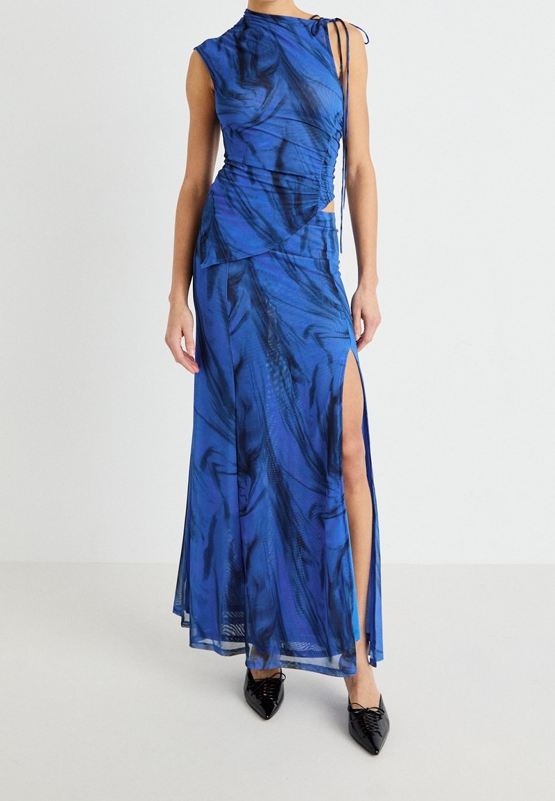 Niebieska sukienka z abstrakcyjnym wzorem, dopasowanym gorsetem, rozcięciami po bokach i asymetrycznym dołem. Wykonana z lekkiego materiału, z detalami w postaci troczków.