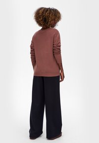 Brązowy sweter z dzianiny z długimi rękawami i okrągłym dekoltem, w zestawieniu z luźnymi czarnymi spodniami o szerokich nogawkach. Teksturowany materiał, swobodny krój.