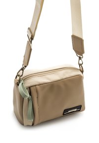 Bolso bandolera beige hecho de material sintético liso. Cuenta con una cremallera superior, correa ajustable y un tirador de cremallera verde. Logo en el frente.