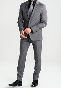 Grå kostym med skräddarsydd passform, med enbladsblazer, notch-revers och raka byxor. Matchad med en svart skjorta och mönstrat slips.