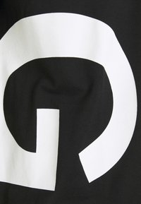 Sort stof med en stor, fed hvid abstrakt geometrisk form, der ligner en del af en spiral eller en roteret "G", trykt på det.