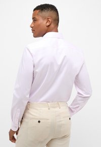 Camicia a maniche lunghe color lilla con colletto classico, texture liscia e polsini abbottonati, abbinata a pantaloni beige.