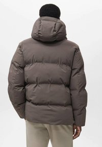 Giacca a vento marrone con cappuccio, caratterizzata da un design trapuntato e un'imbottitura spessa. La parte posteriore mostra una texture liscia e un collo rotondo.