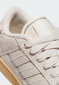 Bijela tenisica od kože i brušene kože, s teksturiranim detaljima, pletenim vezicama i gumenim potplatom s diskretnim uzorkom.