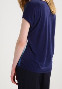Camiseta de color azul marino con mangas cortas, de tejido suave, que presenta un diseño en degradado en los paneles laterales y un ajuste relajado.
