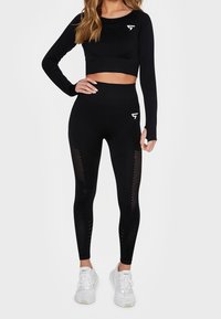 Černý sportovní crop top a legíny s vysokým pasem, které mají texturované panely a výřezy, doplněné bílými teniskami.