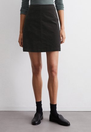 Schwarzer Jeansrock mit taillierter Passform, knielang, mit einer vorderen Naht und einem einfachen Saum. Kombiniert mit schwarzen Slippern und dunklen Socken.