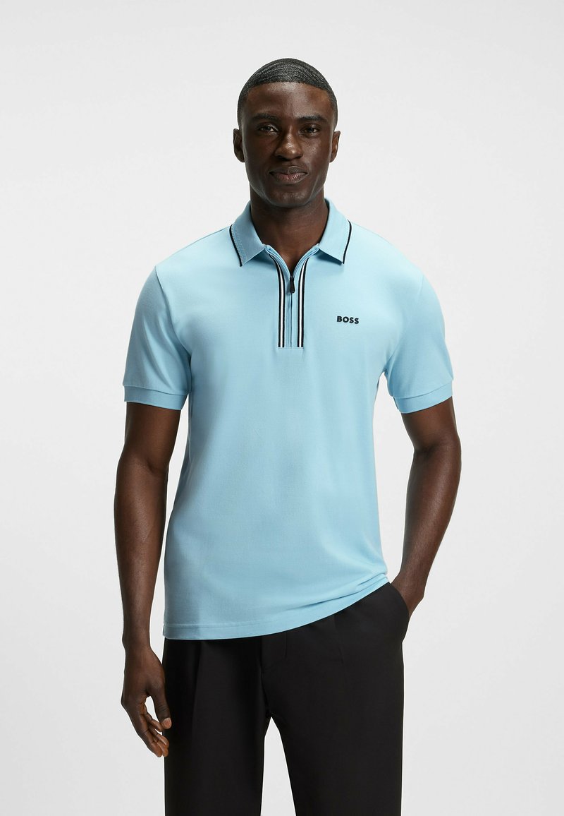 Ljusa blå polo med dragkedja, svarta detaljer och BOSS-logotyp på bröstet. Tillverkad av mjukt, andningsbart material.