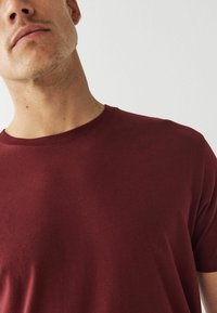 Bordeaux t-shirt med kortærmer lavet af bomuld, med rund halsudskæring og en glat overflade, vist på en ensfarvet lys baggrund.