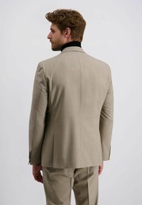 Beige Anzugjacke mit strukturiertem Finish, scharfen Revers und einem doppelten Schlitz hinten. Kombiniert mit passenden Hosen, die eine taillierte Passform aufweisen.