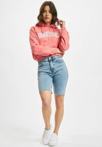 Rosa cropped hettegenser med teksten "SUNKISSED", parret med høyt midje, lyseblå denimshorts. Modellen har på seg hvite sneakers.