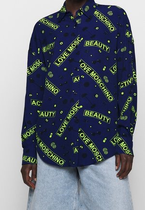 Dark blue button-up shirt with neon green "LOVE MOSCHINO," "BEAUTY," and "ACTIVITY" text and small black graphic icons, worn with light jeans.