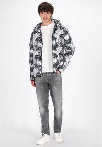 Giacca con cappuccio con motivo marmorizzato bianco e nero, chiusura a zip frontale, polsini elasticizzati, abbinata a jeans grigi e sneaker bianche, in piedi su uno sfondo neutro.