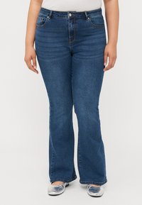 Vaqueros de mezclilla acampanados en azul oscuro con una cintura de altura media, que presentan un diseño estándar de cinco bolsillos y detalles de costura sutiles. Textura suave.