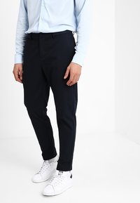 Pantalon marine ajusté, fabriqué en tissu tissé. Il dispose de poches latérales et de passants de ceinture. Assorti à des baskets blanches pour le contraste.