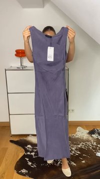 Vestido longo e sem mangas em tecido roxo suave com silhueta reta. Apresenta uma etiqueta presa ao decote e uma fenda lateral.