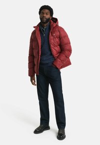 Rote Daunenjacke mit Kapuze, gestepptes Muster, marineblaues Sweatshirt darunter, dunkle Jeans und schwarze Schnürstiefel. Schlichtes Design und lässige Passform.