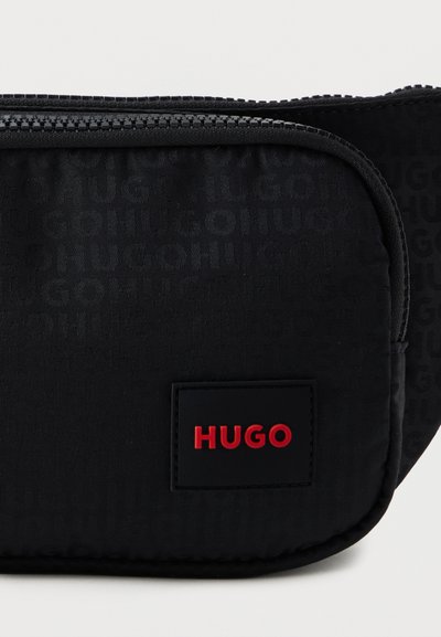Pochette noire zippée avec un motif de texte répétitif "HUGO" et un patch noir avec "HUGO" en lettres rouges à l'avant.
