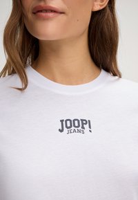 Weißes Baumwoll-T-Shirt mit einem schwarzen "JOOP! JEANS" Logo über der Brust. Runder Ausschnitt und weicher Stoff. Einfaches, lässiges Design.