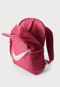 Roza Nike nahrbtnik z velikim belim logotipom, ki ima zadrge, nastavljive naramnice in teksturirano tkanino.