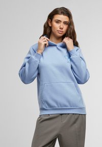 Lyseblå hettegenser med frontlomme, snor til hetten og blå blomsterdesigndetaljer på brystet. Stoffet ser mykt ut med en jevn tekstur.