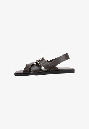 Sandale plate marron foncé avec des brides en cuir croisées et une boucle argentée réglable sur le côté, bout ouvert et design à bride arrière.