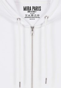 Felpa con zip bianca in cotone, dotata di zip metallica, cordini e un'etichetta con il nome del marchio, le istruzioni per la cura e il logo sul collo.