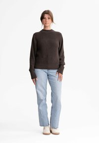 Dunkelbrauner, gestrickter Pullover mit Rundhalsausschnitt, geripptem Muster und langen Ärmeln, kombiniert mit hellblauen, geraden Jeans und cremefarbenen Sneakers.