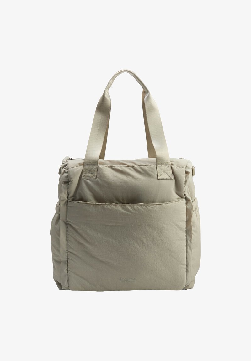Beżowa torba tote z wypełnieniem, z dwiema materiałowymi uchwytami, przednią kieszenią i teksturowaną powierzchnią. Charakteryzuje się minimalistycznym wzornictwem bez widocznych metalowych elementów.
