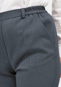 Dunkelgraue maßgeschneiderte Hose aus strukturiertem Stoff mit elastischem Bund und seitlichen Taschen, die sich durch klare Linien und eine taillierte Silhouette auszeichnet.