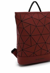 Punainen geometrisilla kuvioilla varustettu reppu, joka on valmistettu sileästä materiaalista mustilla yksityiskohdilla. Varustettu yläkahvalla ja säädettävillä olkahihnoilla.